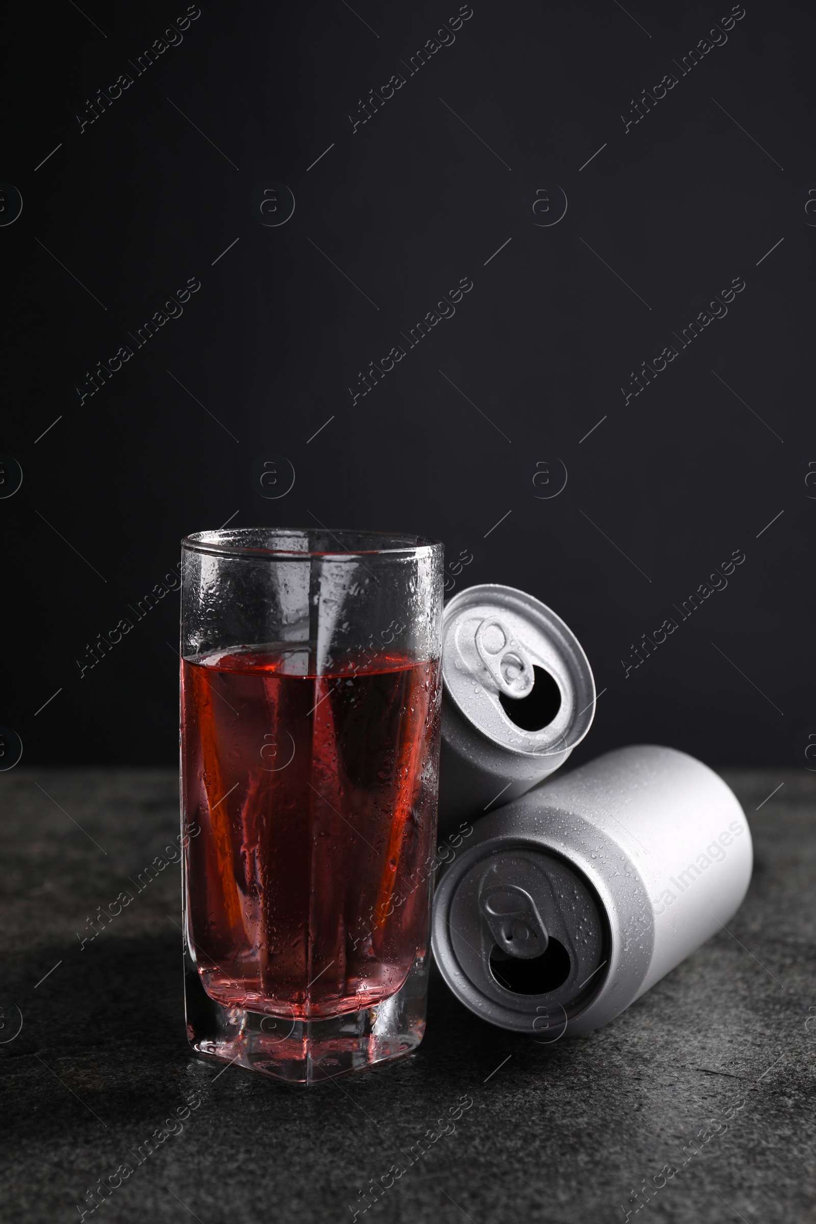 Photo of Energy drink in glass and aluminium cans on grey table