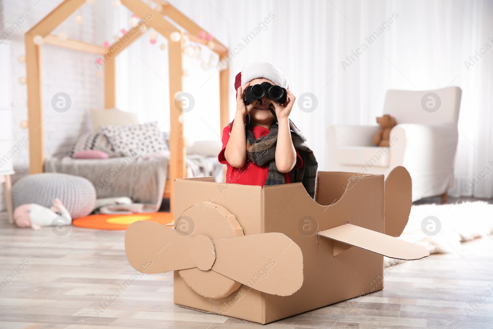 Photo of Cute little boy playing with binoculars and cardboard airplane in bedroom