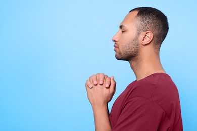 Photo of African American man with clasped hands praying to God on light blue background. Space for text