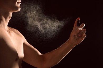 Image of Young man applying perfume on black background, closeup