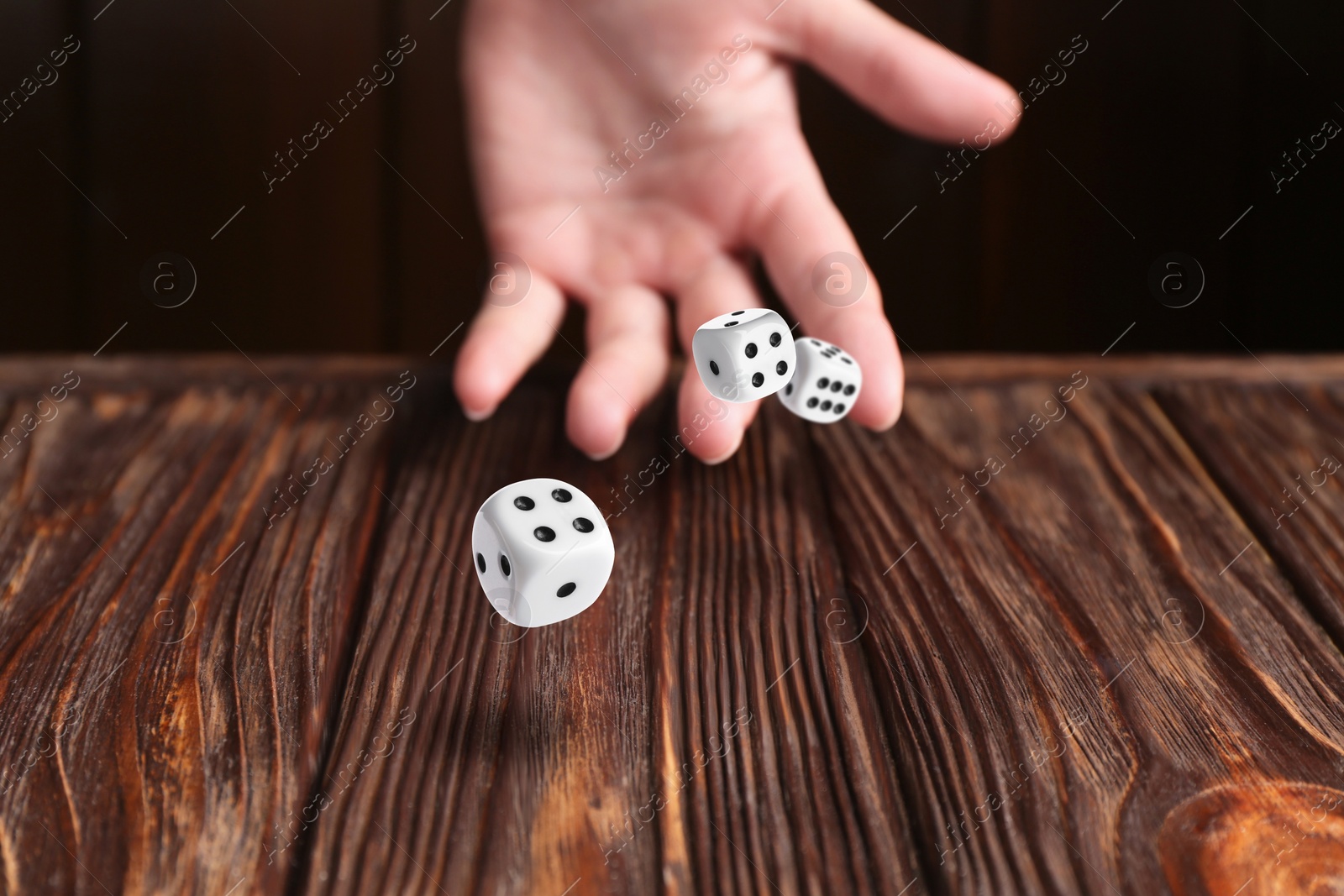 Image of Woman throwing white dice on wooden table, closeup