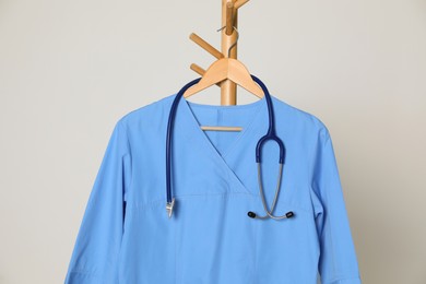 Photo of Medical uniform and stethoscope hanging on rack against light grey background