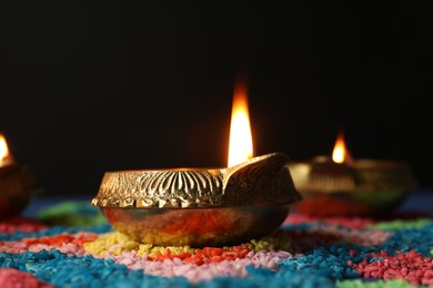 Photo of Diwali celebration. Diya lamps and colorful rangoli on table against black background, closeup