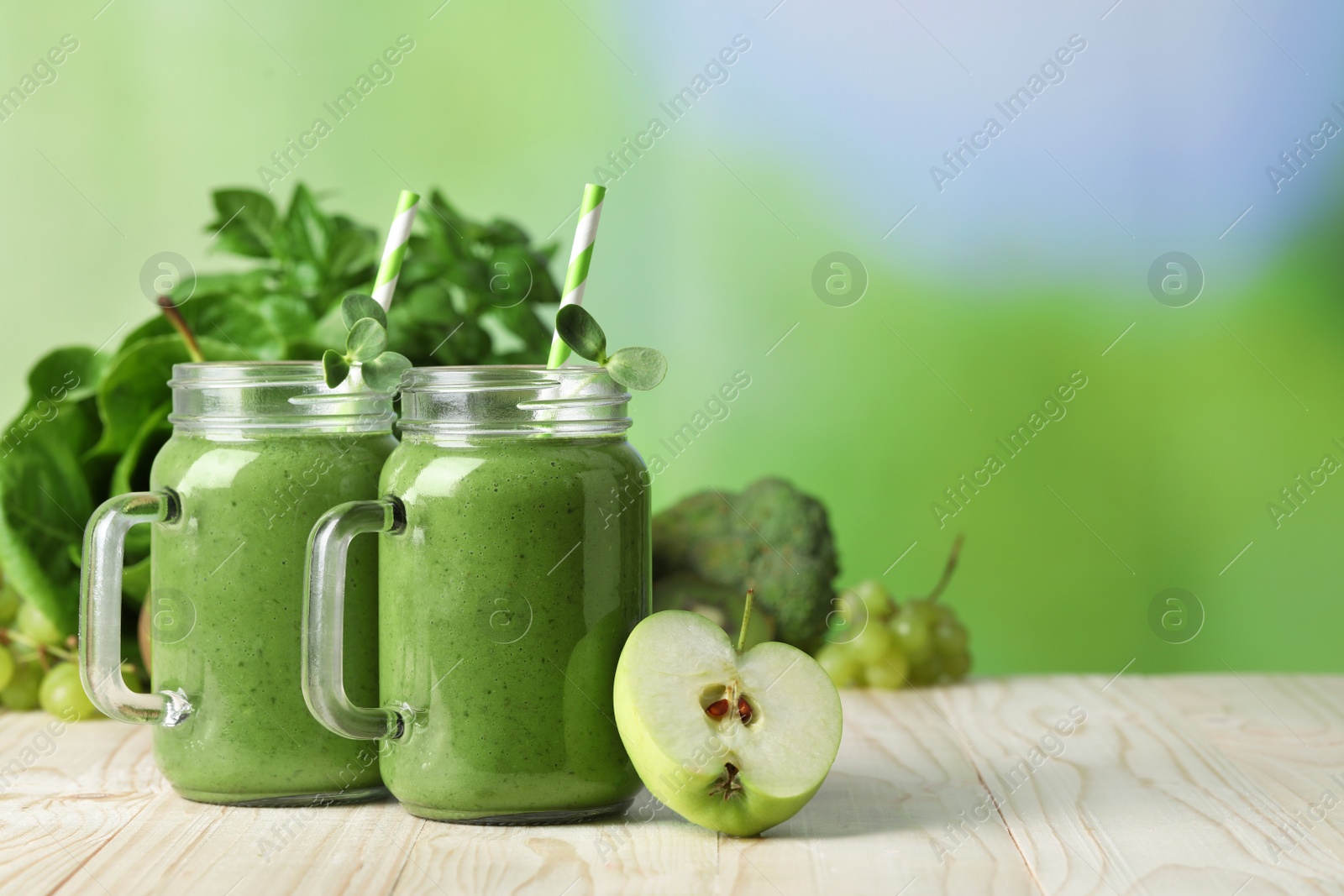 Photo of Mason jars of fresh green smoothie and ingredients on wooden table, space for text