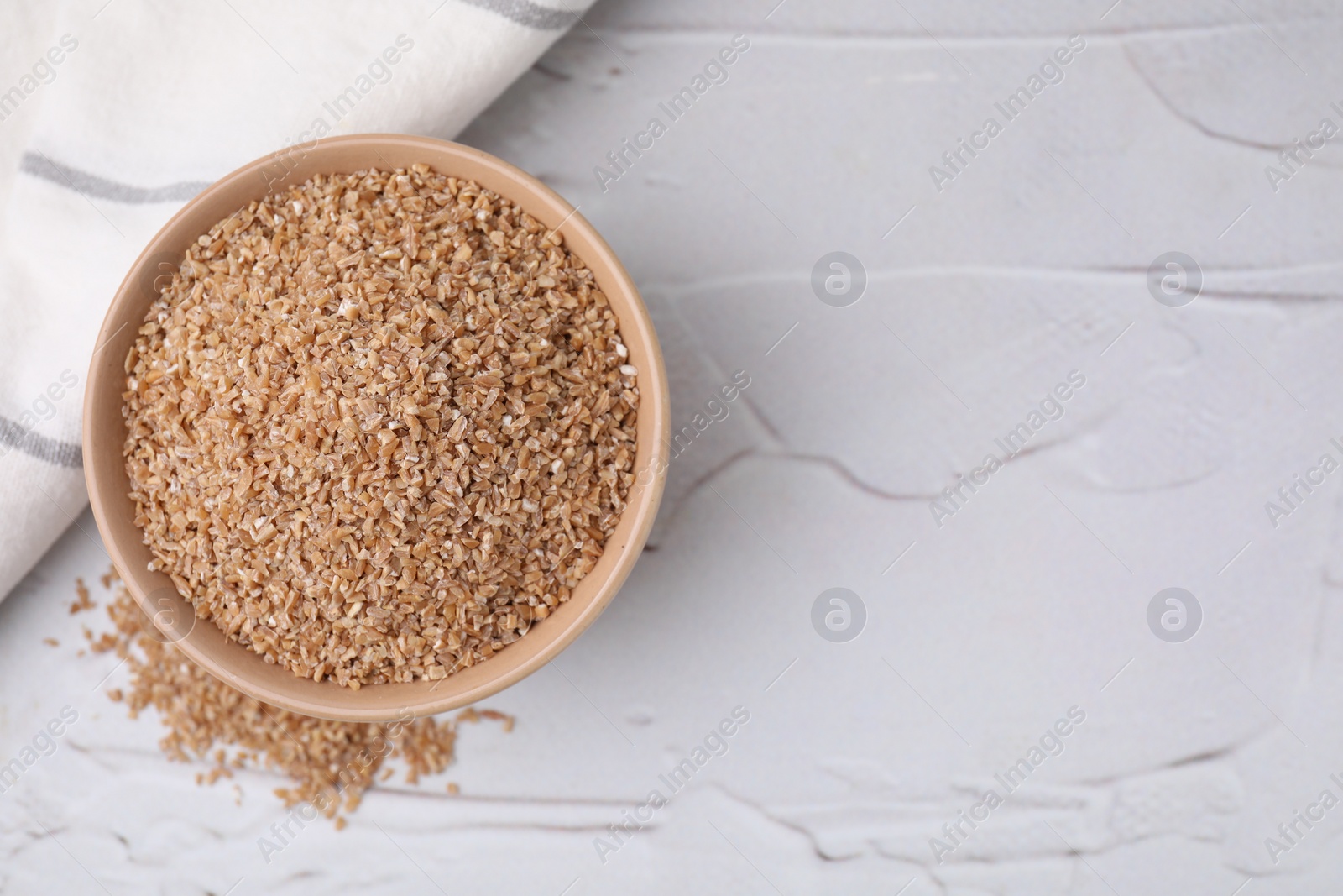 Photo of Dry wheat groats in bowl on light textured table, top view. Space for text