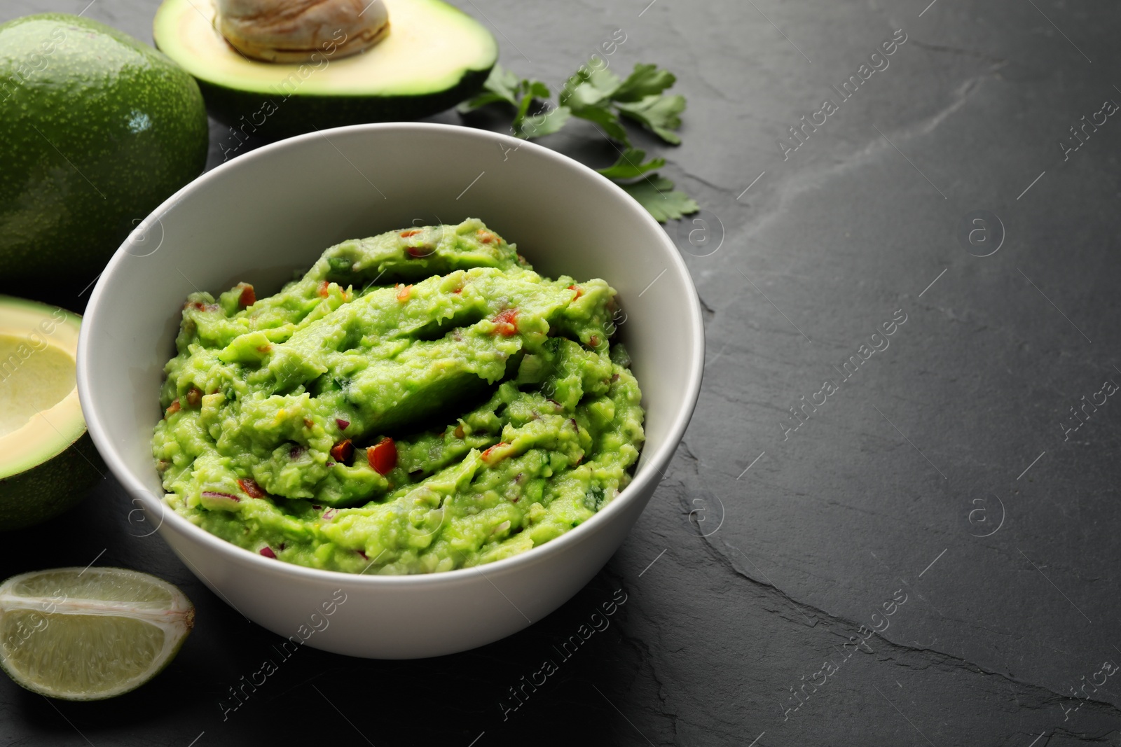 Photo of Delicious guacamole, fresh avocado and parsley on grey table. Space for text