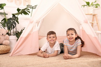 Cute little children in toy wigwam at home