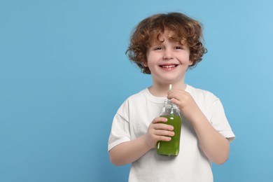 Photo of Cute little boy with glass bottle of fresh juice on light blue background, space for text