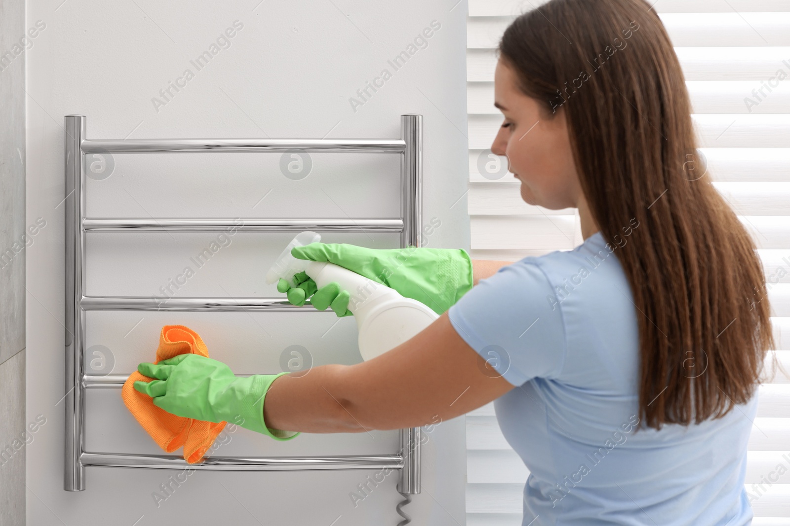 Photo of Woman cleaning heated towel rail with sprayer and rag