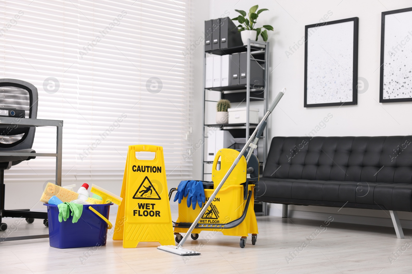 Photo of Cleaning service. Mop, wet floor sign and bucket with supplies in office