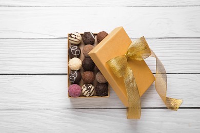 Photo of Open box with delicious chocolate candies on white wooden table, top view