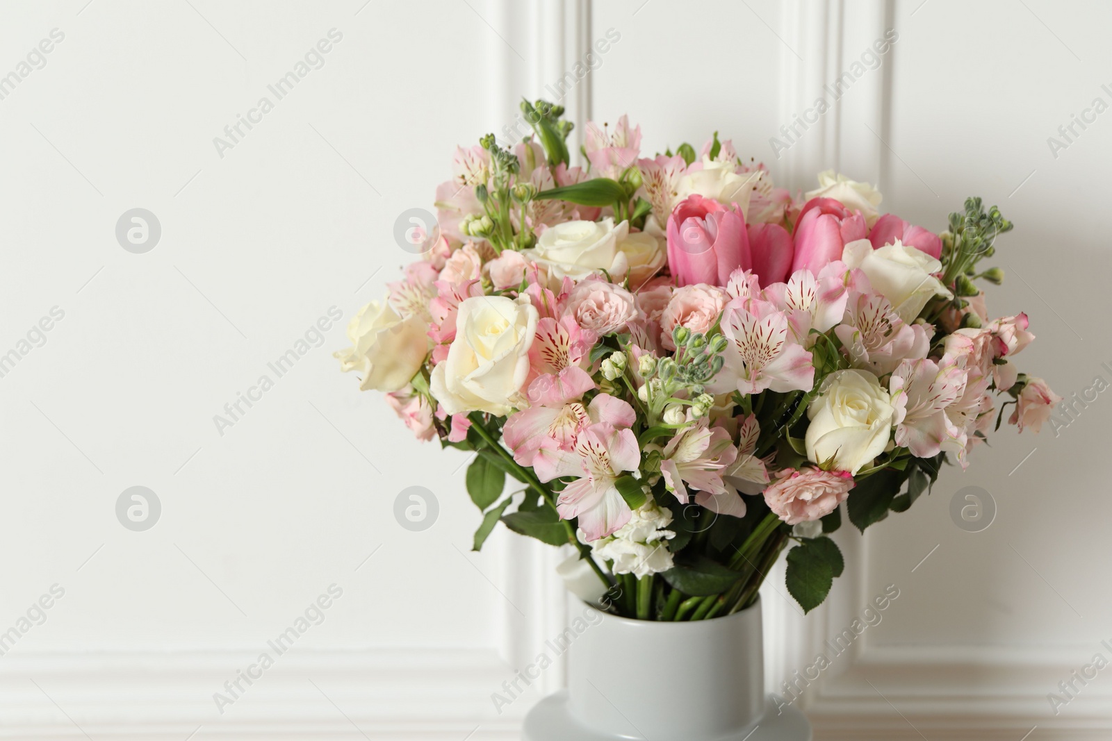 Photo of Beautiful bouquet of fresh flowers in vase near white wall, space for text