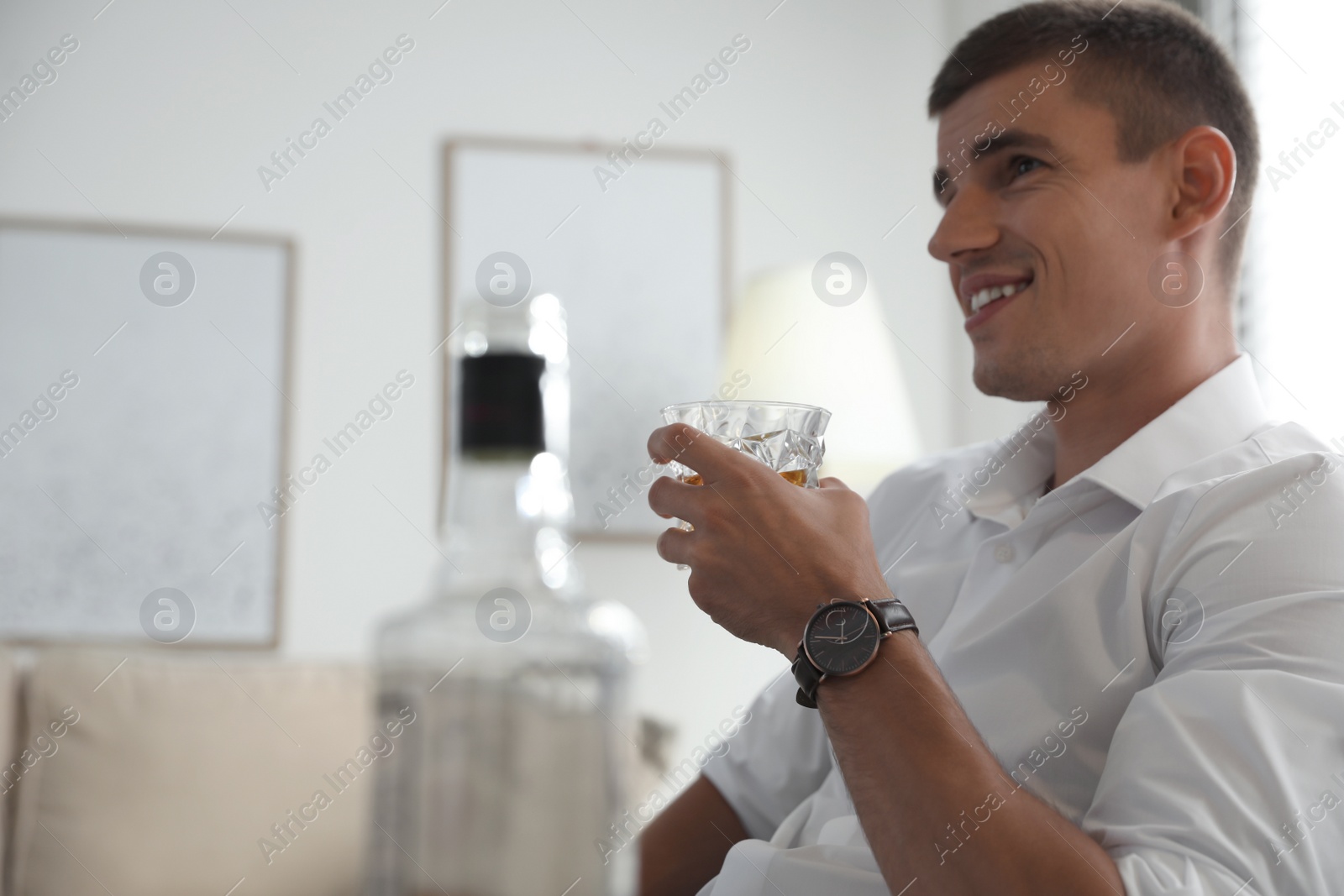 Photo of Young man with glass of whiskey at home. Space for text