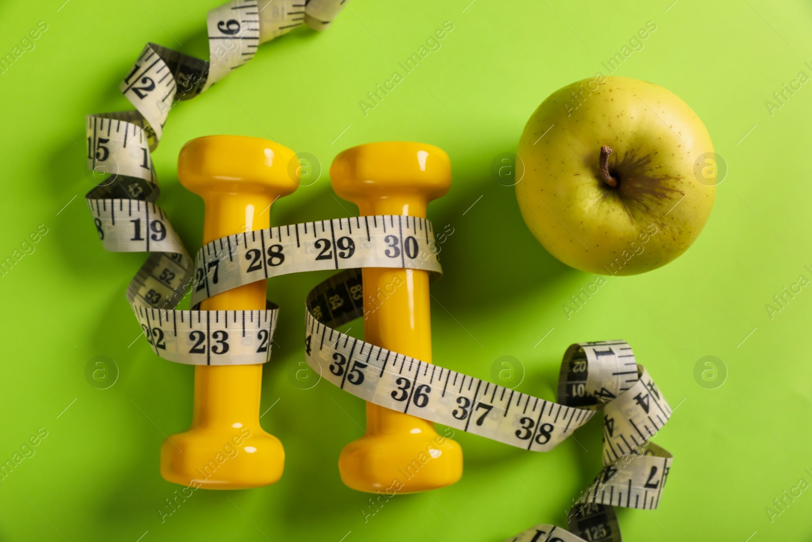 Photo of Measuring tape, dumbbells and apple on light green background, flat lay. Weight control concept