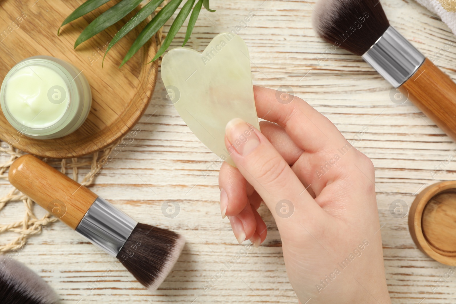 Photo of Woman with jade gua sha tool at white wooden table, top view