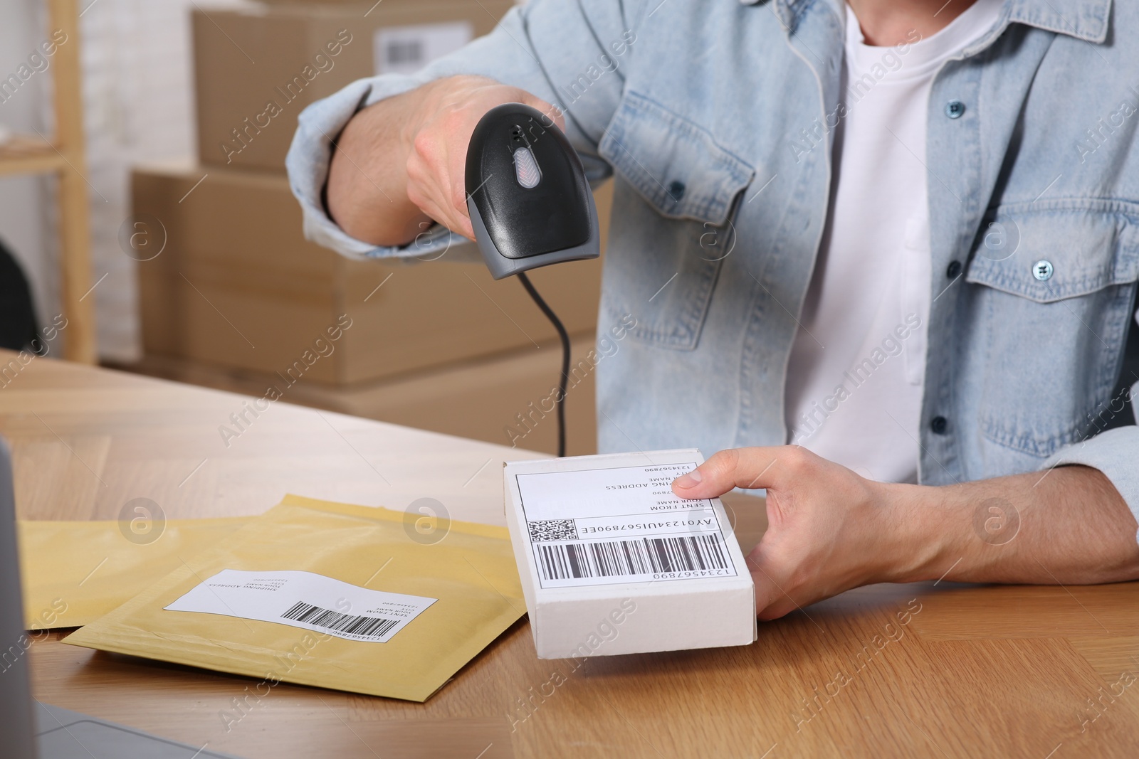 Photo of Seller with scanner reading parcel barcode at table in office, closeup. Online store