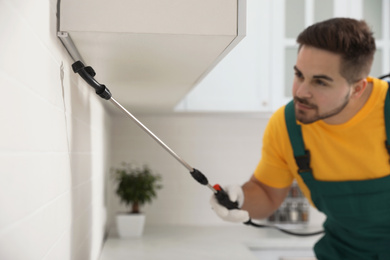 Photo of Pest control worker spraying insecticide on furniture in kitchen, focus on device