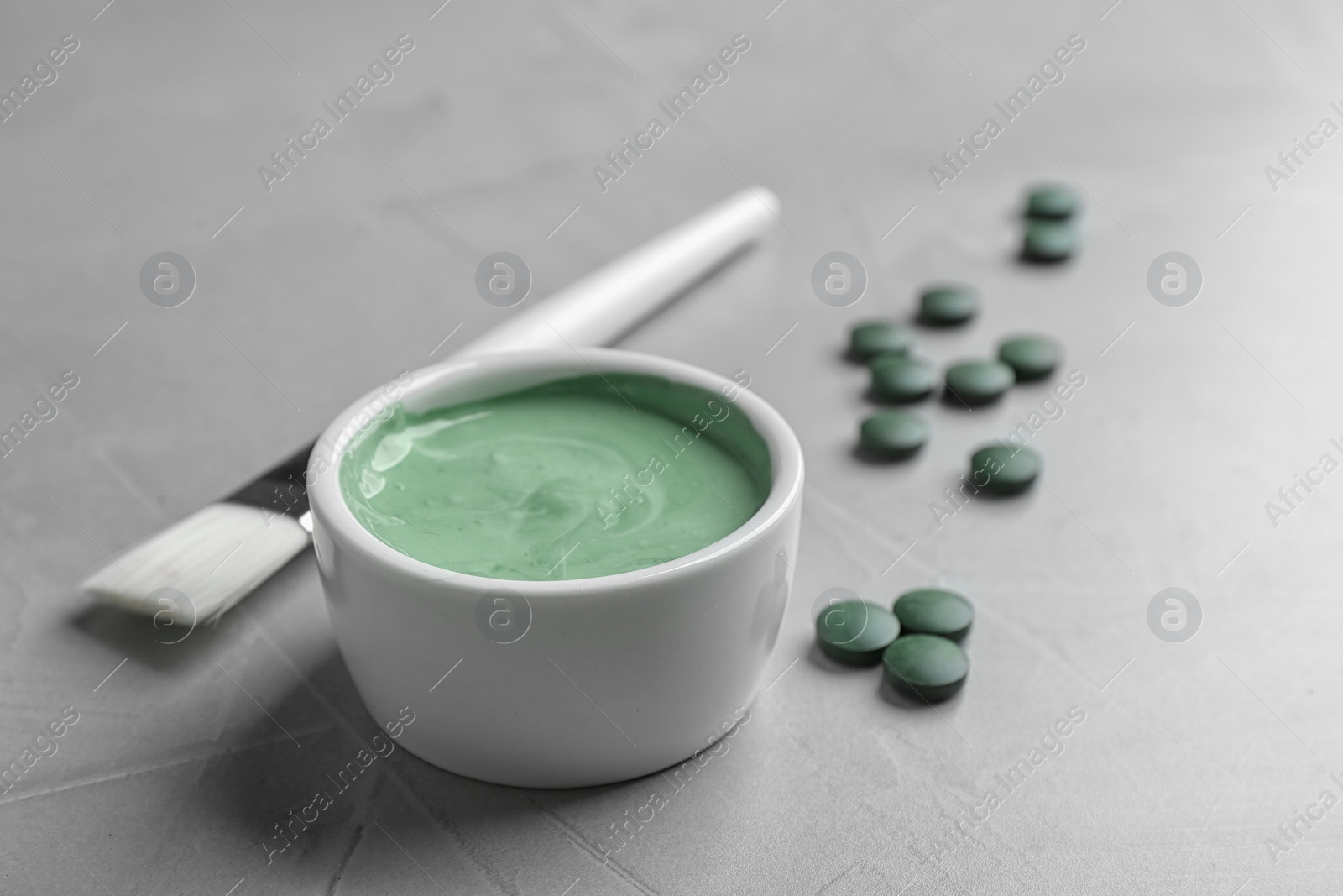 Photo of Freshly made spirulina in bowl, pills and brush on light grey table