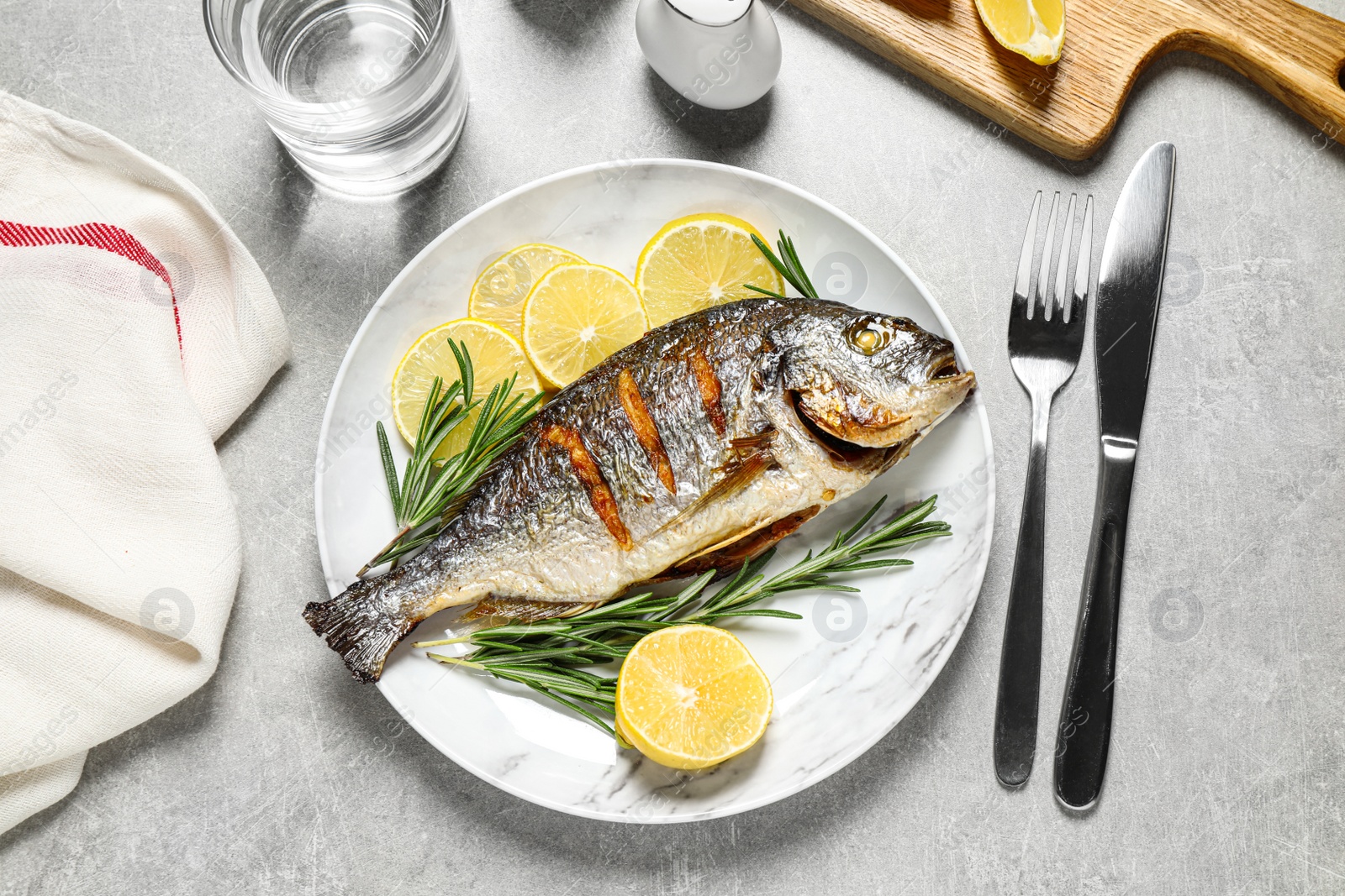 Photo of Delicious roasted fish with lemon on grey table, flat lay