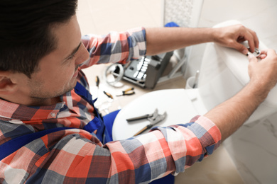 Photo of Professional plumber working with toilet bowl in bathroom, closeup