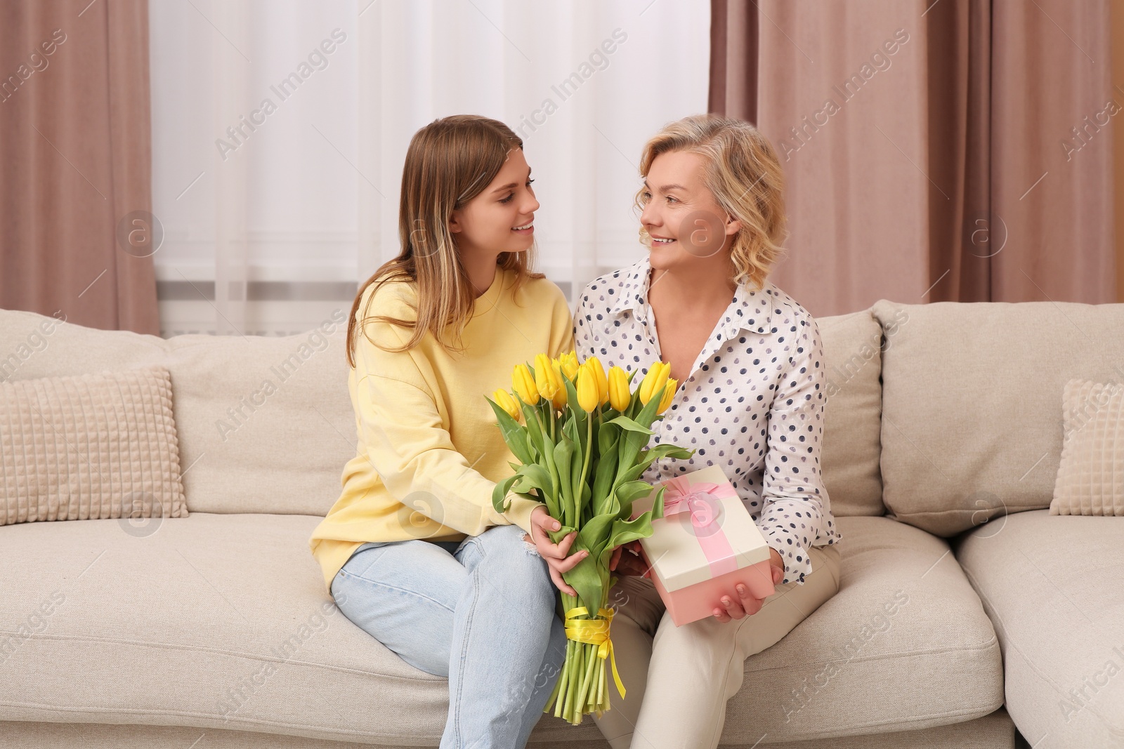 Photo of Young daughter congratulating her mom with flowers and gift at home. Happy Mother's Day