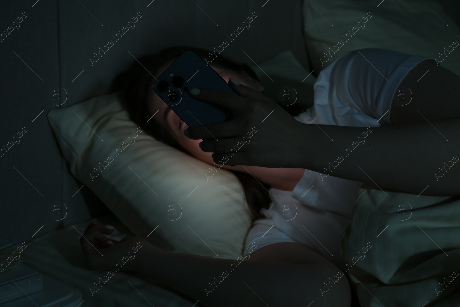 Photo of Woman using smartphone on bed at night. Internet addiction