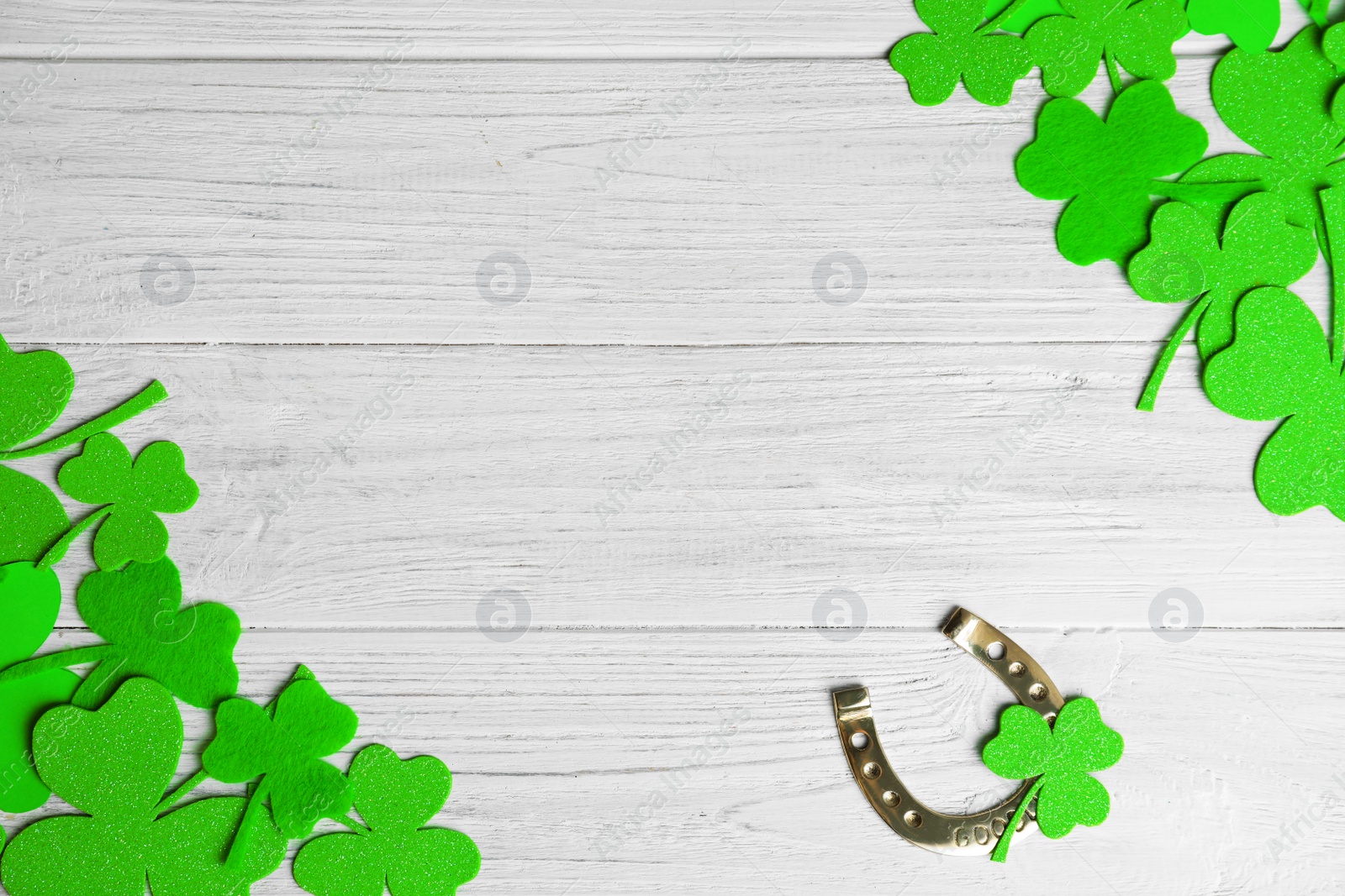 Photo of Frame made of clover leaves and horseshoe on white wooden background, flat lay with space for text. St. Patrick's day