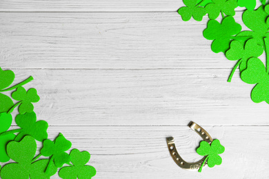 Photo of Frame made of clover leaves and horseshoe on white wooden background, flat lay with space for text. St. Patrick's day