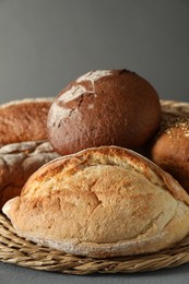 Wicker basket with different types of fresh bread on grey table, closeup