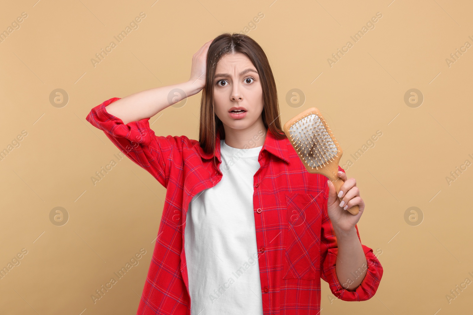 Photo of Emotional woman holding brush with lost hair on beige background. Alopecia problem