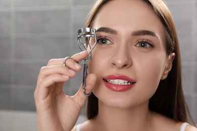 Young woman using eyelash curler indoors, closeup