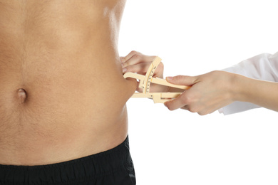 Photo of Nutritionist measuring man's body fat layer with caliper on white background, closeup