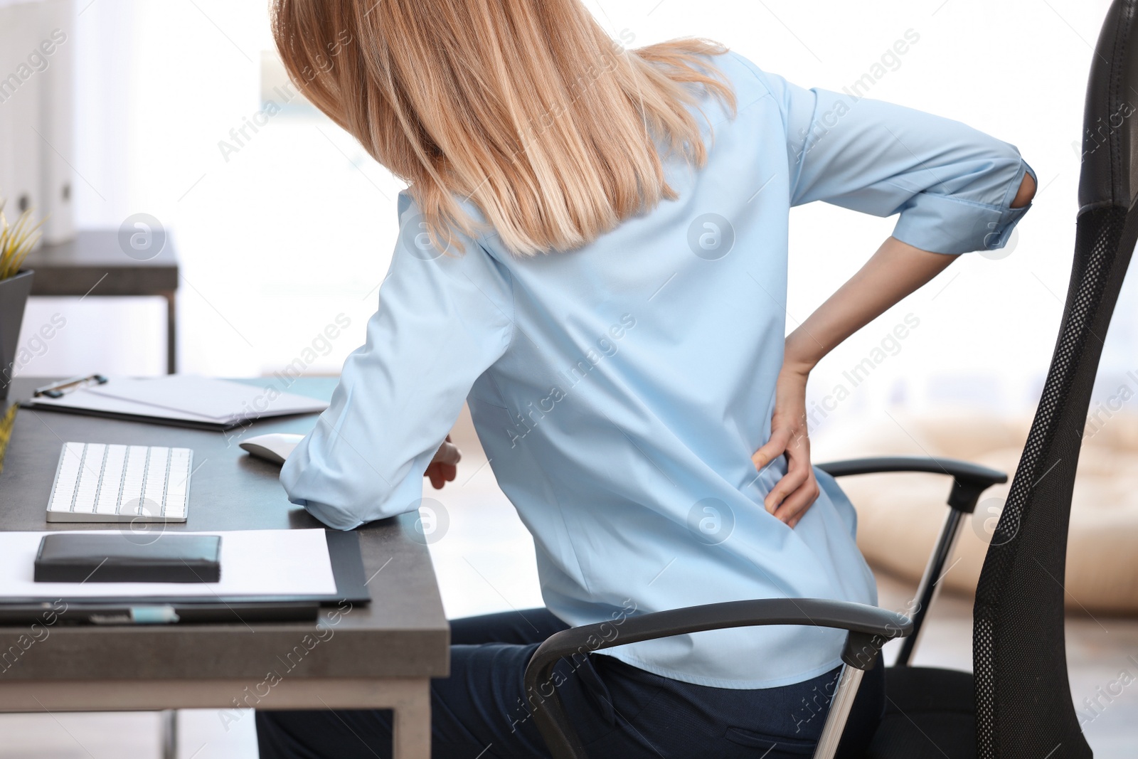 Photo of Young woman suffering from back pain in office