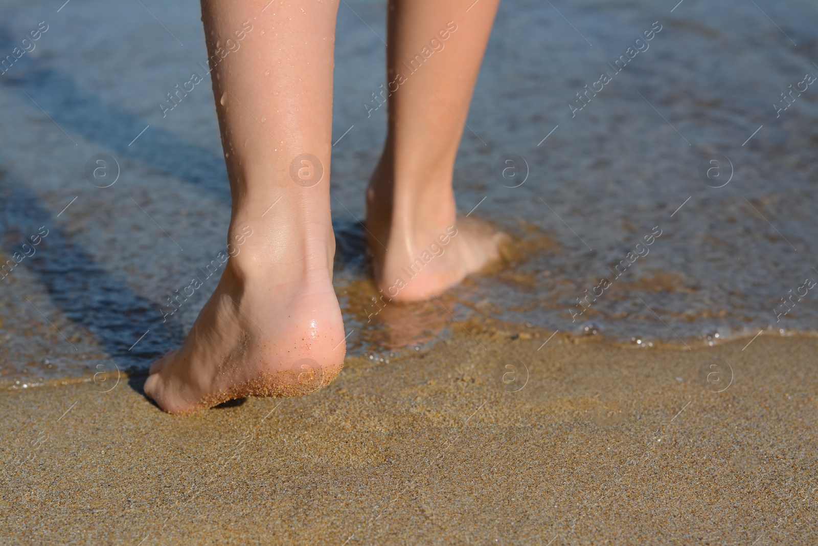 Photo of Child walking through water on seashore, closeup of legs. Space for text