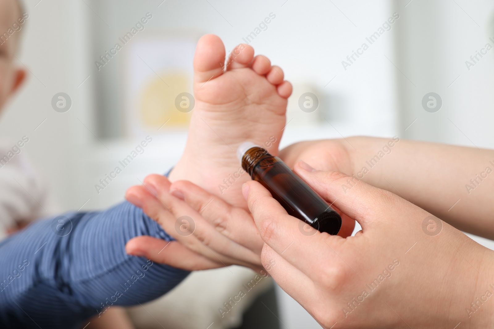 Photo of Mother applying essential oil from roller bottle onto her baby`s heel indoors, closeup