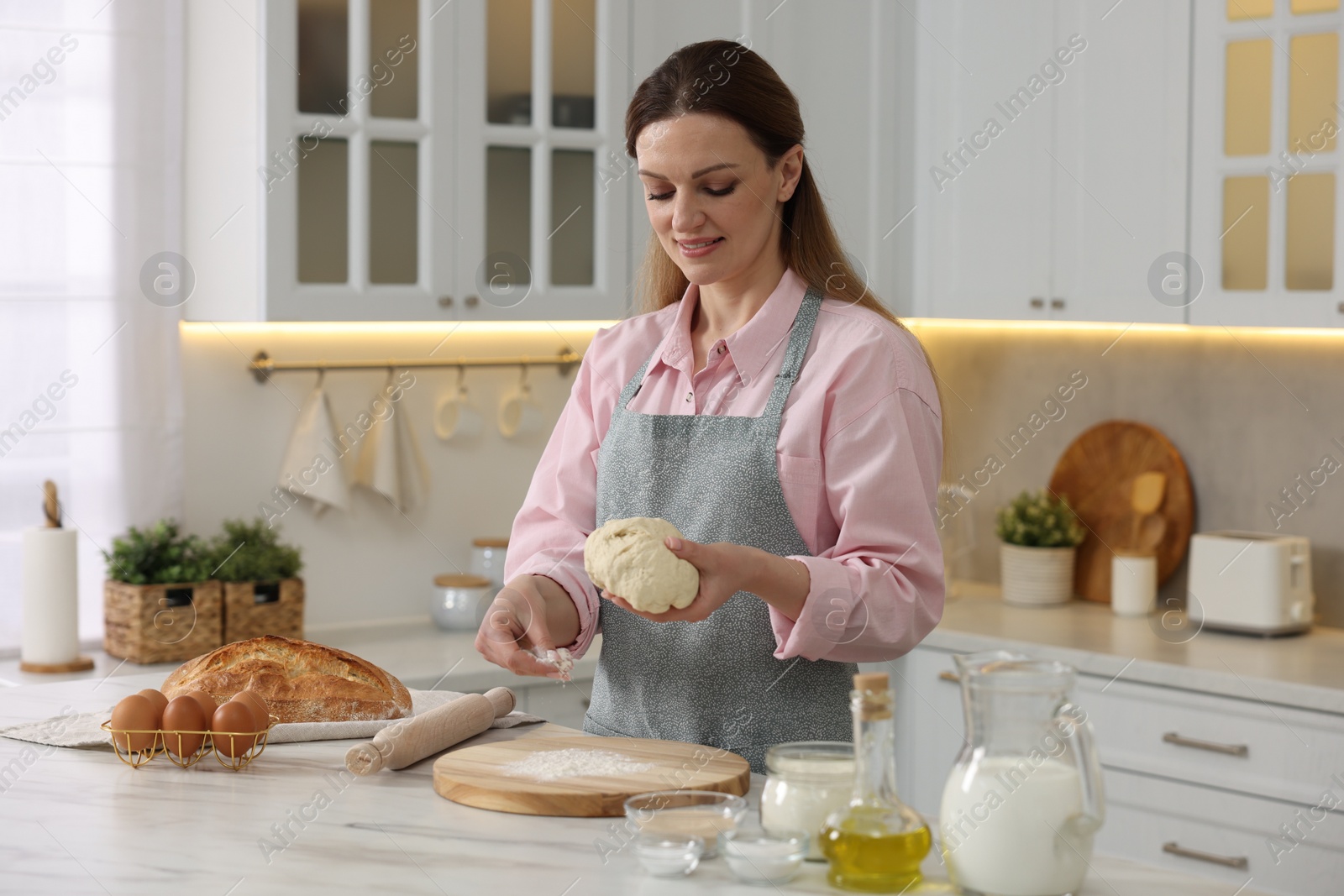 Photo of Making bread. Woman preparing raw dough at white table in kitchen
