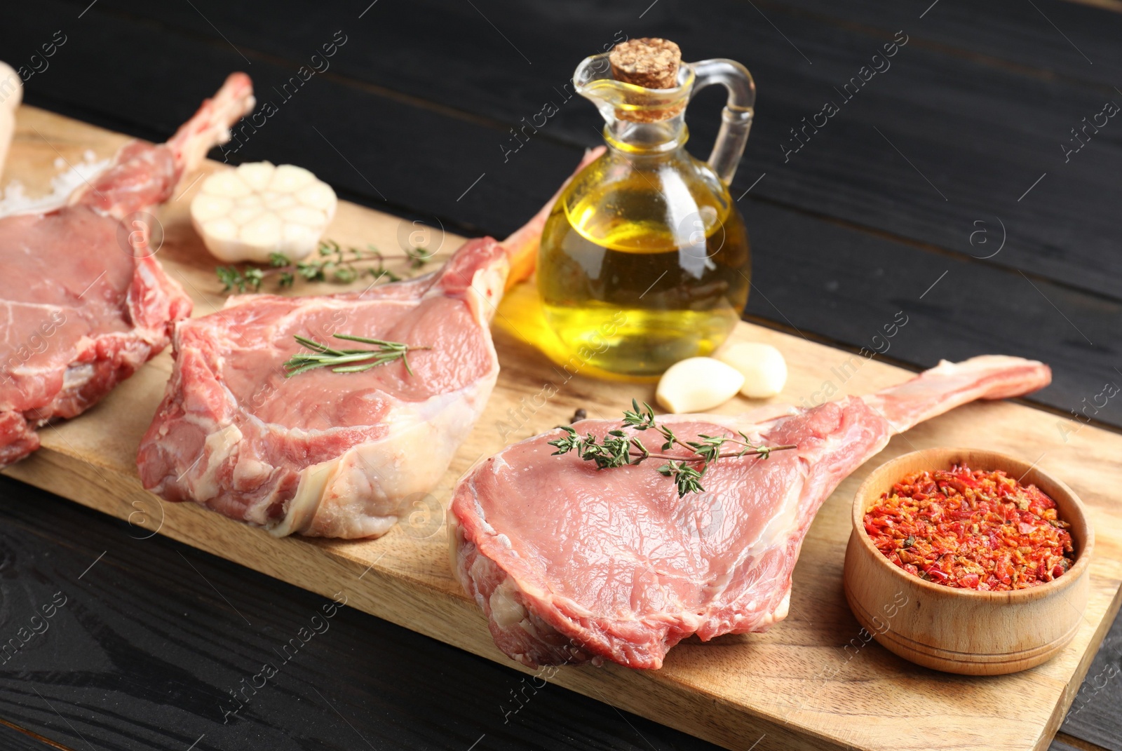 Photo of Fresh tomahawk beef cuts, spices and oil on black wooden table