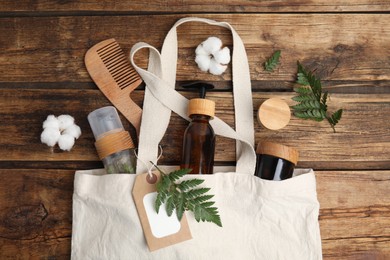 Photo of White cotton bag with eco friendly personal care products on wooden table, flat lay