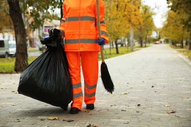 Photo of Street cleaner with broom and garbage bag outdoors on autumn day, closeup