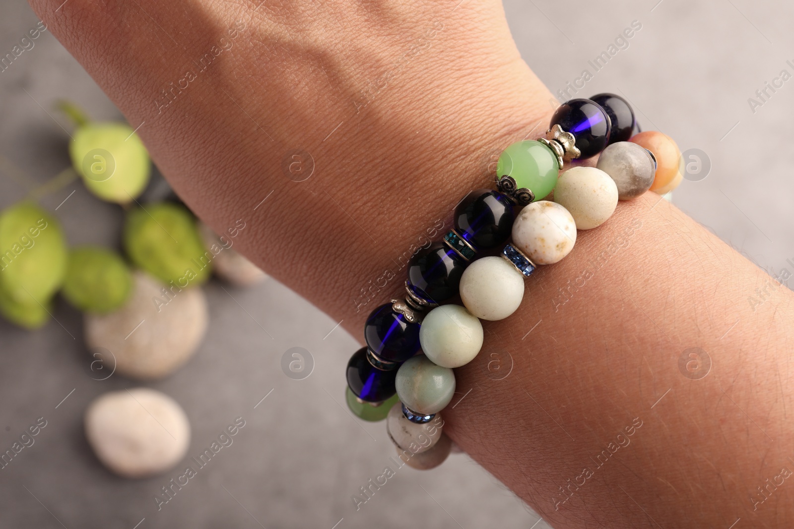 Photo of Woman wearing beautiful bracelets with gemstones on blurred background, closeup