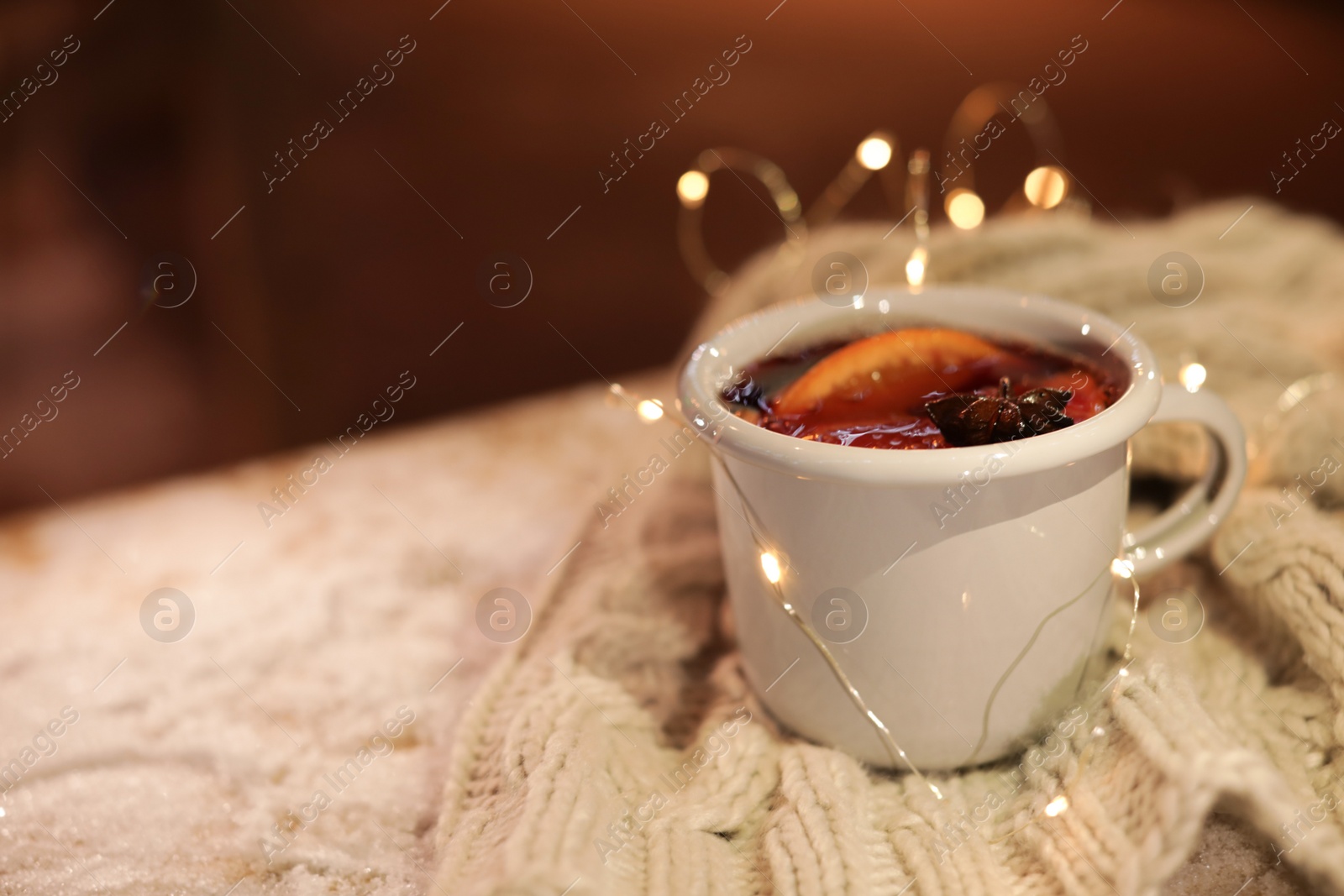 Photo of Cup of hot mulled wine and garland on table against blurred background. Space for text