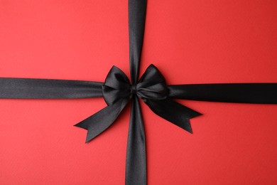 Photo of Black satin ribbon with bow on red background, top view