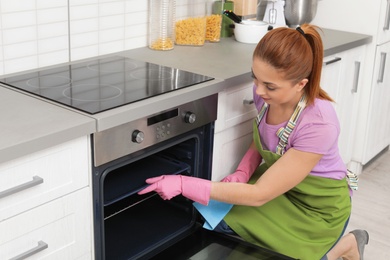 Woman cleaning oven tray with rag in kitchen