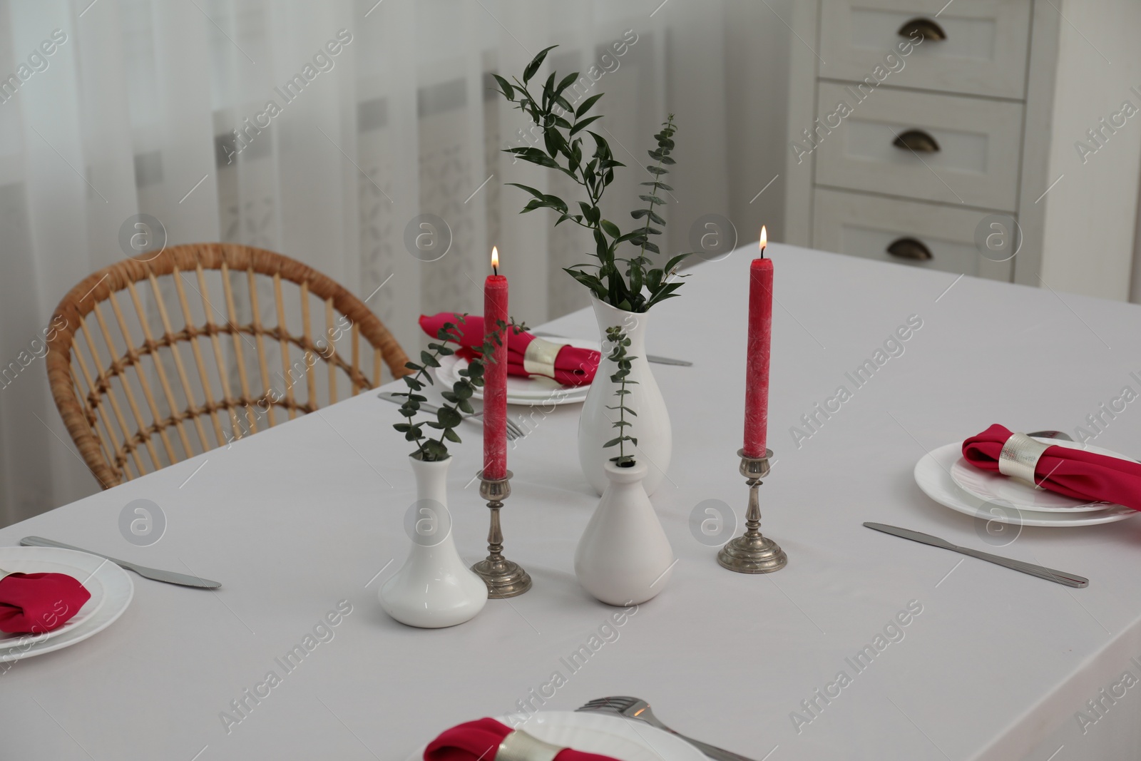 Photo of Beautiful table setting with green branches in vases and burning candles indoors. Stylish dining room