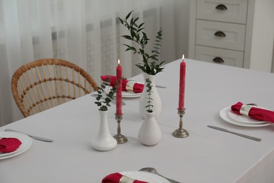 Beautiful table setting with green branches in vases and burning candles indoors. Stylish dining room