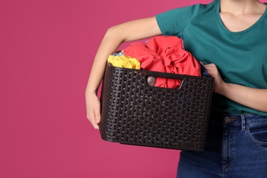 Photo of Young woman holding basket with clothes on color background, closeup. Space for text