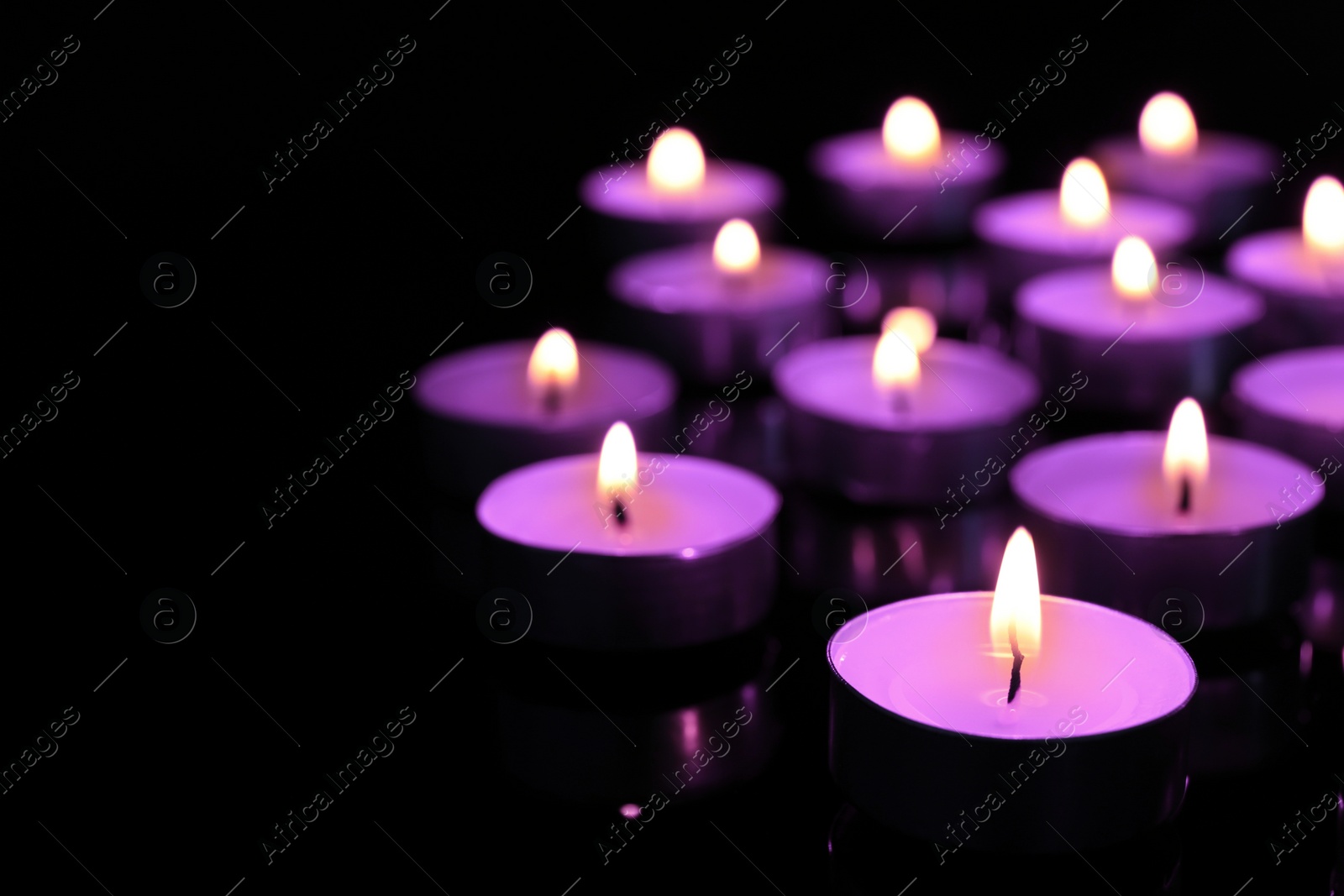 Image of Beautiful burning violet candles on black background. Funeral attributes