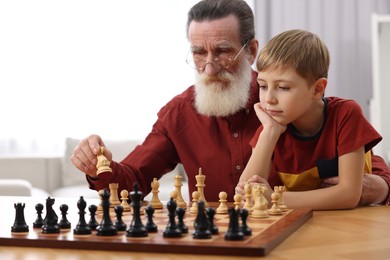 Photo of Senior man teaching his grandson to play chess at home