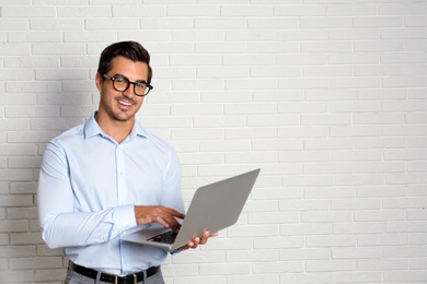 Young male teacher with glasses and laptop near brick wall. Space for text