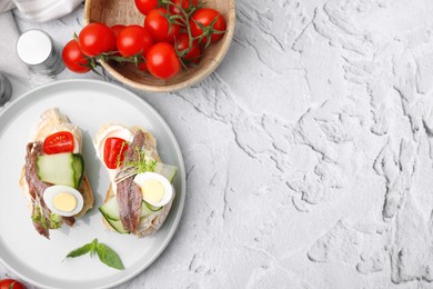 Photo of Delicious bruschettas with anchovies, tomato, cucumber, egg and cream cheese on white textured table, flat lay. Space for text